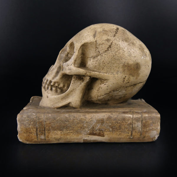 Petit crâne sur vieux livre relié en plâtre patiné Vanité Memento mori (profil)