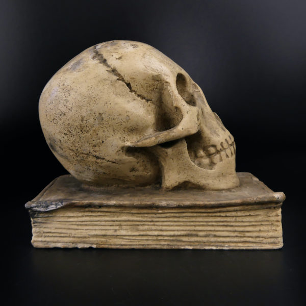 Petit crâne sur vieux livre relié en plâtre patiné Vanité Memento mori (profil)