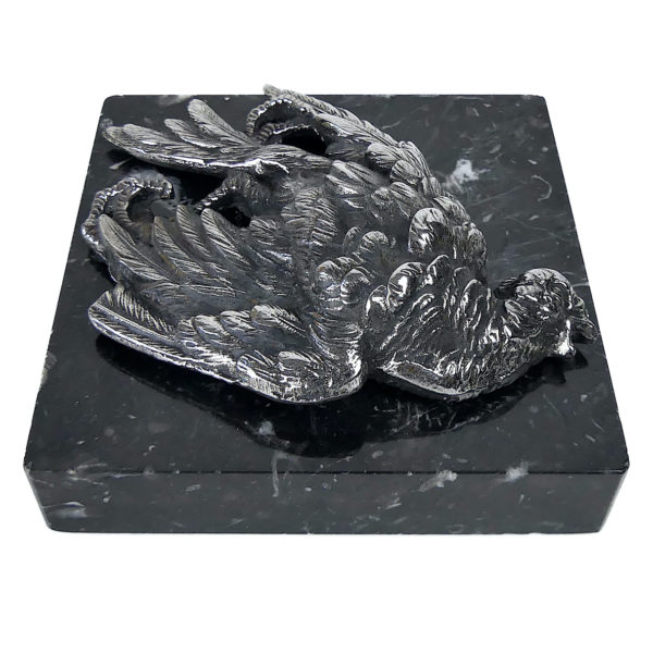 Petit oiseau mort en métal argenté sur plaque carrée de marbre noir (profil 3/4)